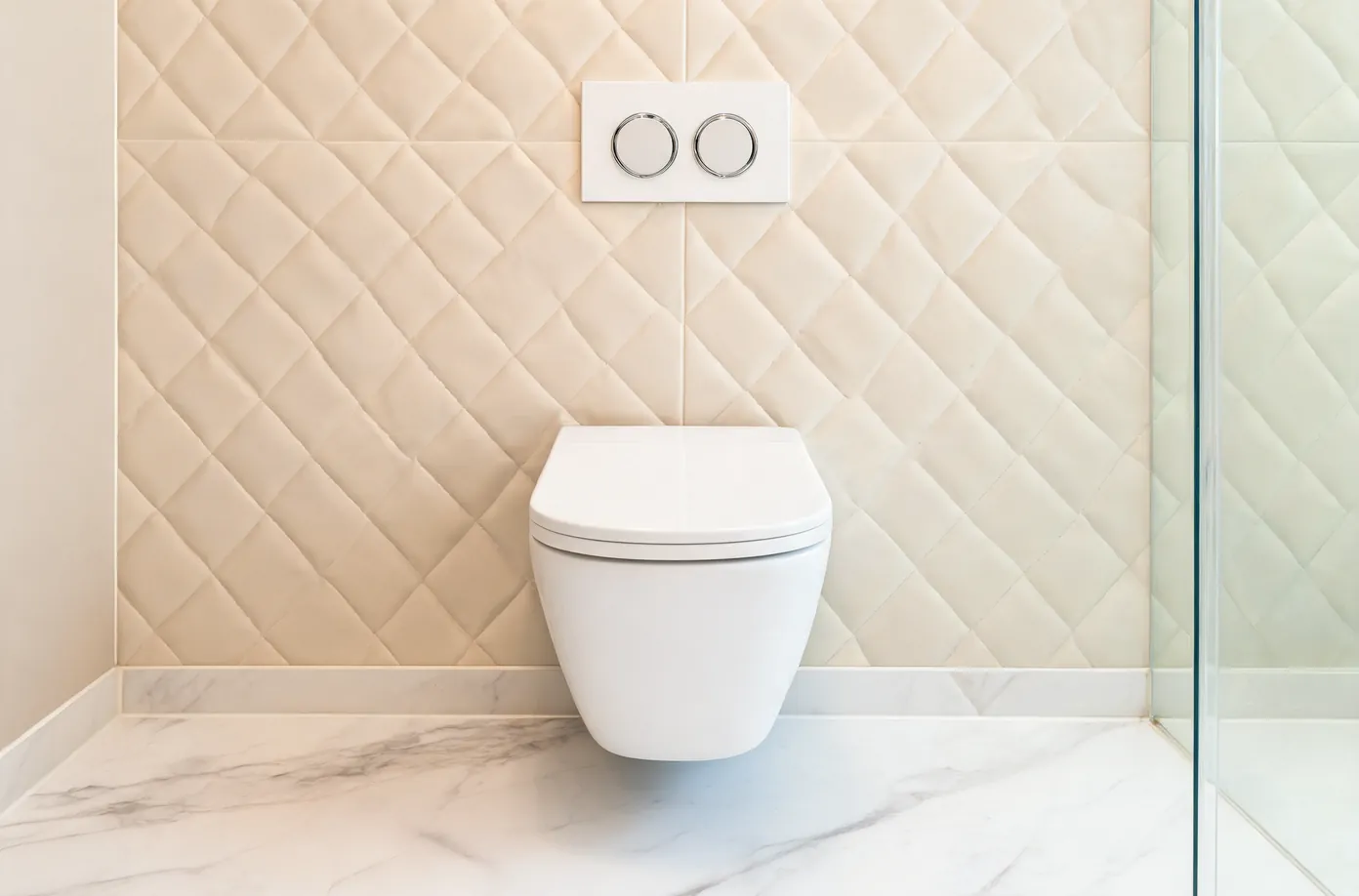 Bej baklava desenli fayanslı banyoda asma klozet ve beyaz çift düğmeli kumanda paneli